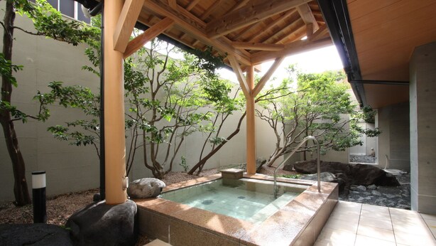 Uma área de spa com hidromassagem, pérgola de madeira e árvores ao redor.