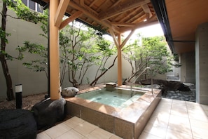 A spa area with a hot tub, wooden pergola, and surrounding trees. - Uozu Manten Hotel Ekimae (Uozu)