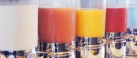 Cuatro dispensadores de vidrio con líquidos de colores diferentes, probablemente zumos o batidos, en un entorno comercial.