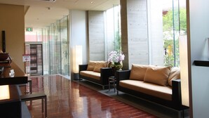 Um lobby moderno com balcão de recepção, área de estar e grandes janelas com vista para o exterior.
