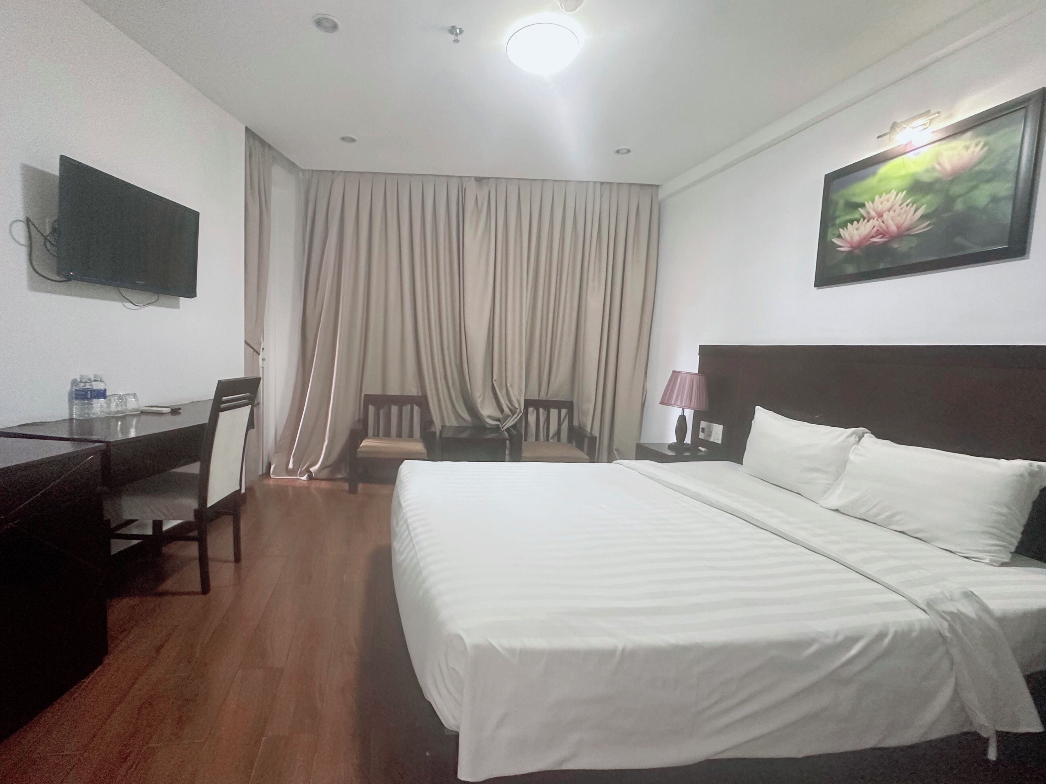A hotel room with a bed, a desk, a chair, a television, and a window with curtains.