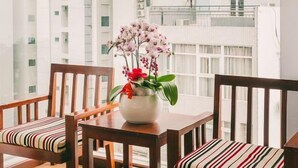 A balcony with a wooden table and chairs, a vase with flowers, and a view of high-rise buildings. - Dragon Sea Hotel (Da Nang)