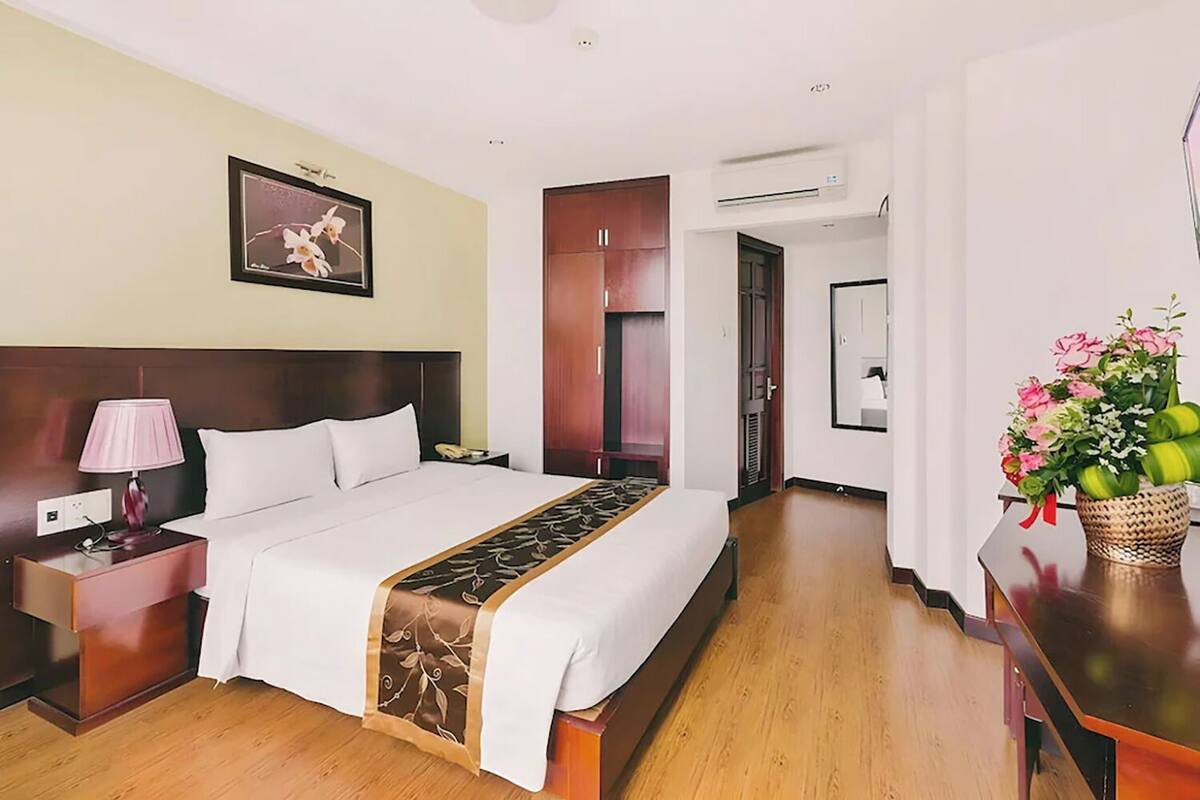 A hotel room with a bed, bedside table, lamp, and a floral arrangement.