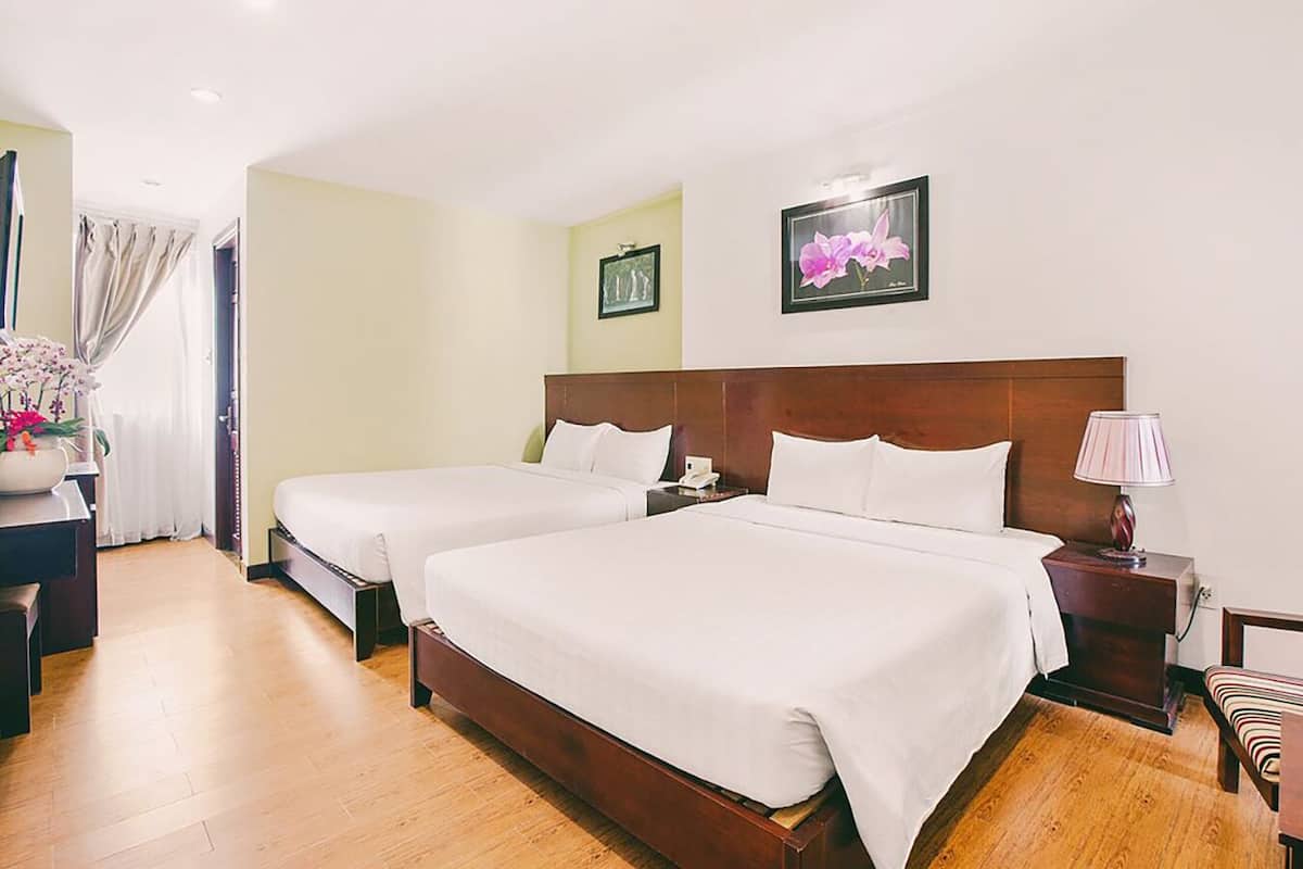 A hotel room with two beds, a wooden floor, a nightstand with a lamp, and a picture on the wall.