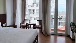 A hotel room with a bed, a small table with chairs, a balcony with curtains, and a view of the cityscape. - Dragon Sea Hotel (Da Nang)