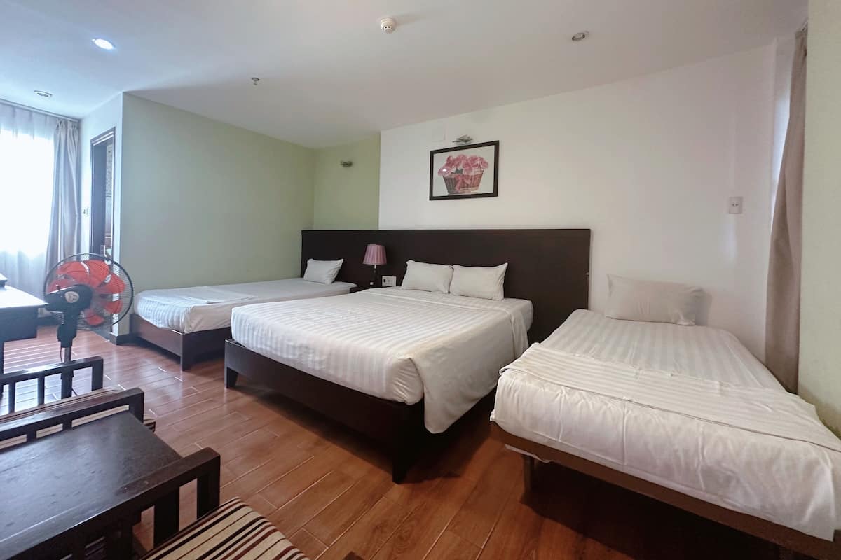 A hotel room with two single beds, a wooden table, a fan, and a window with curtains.