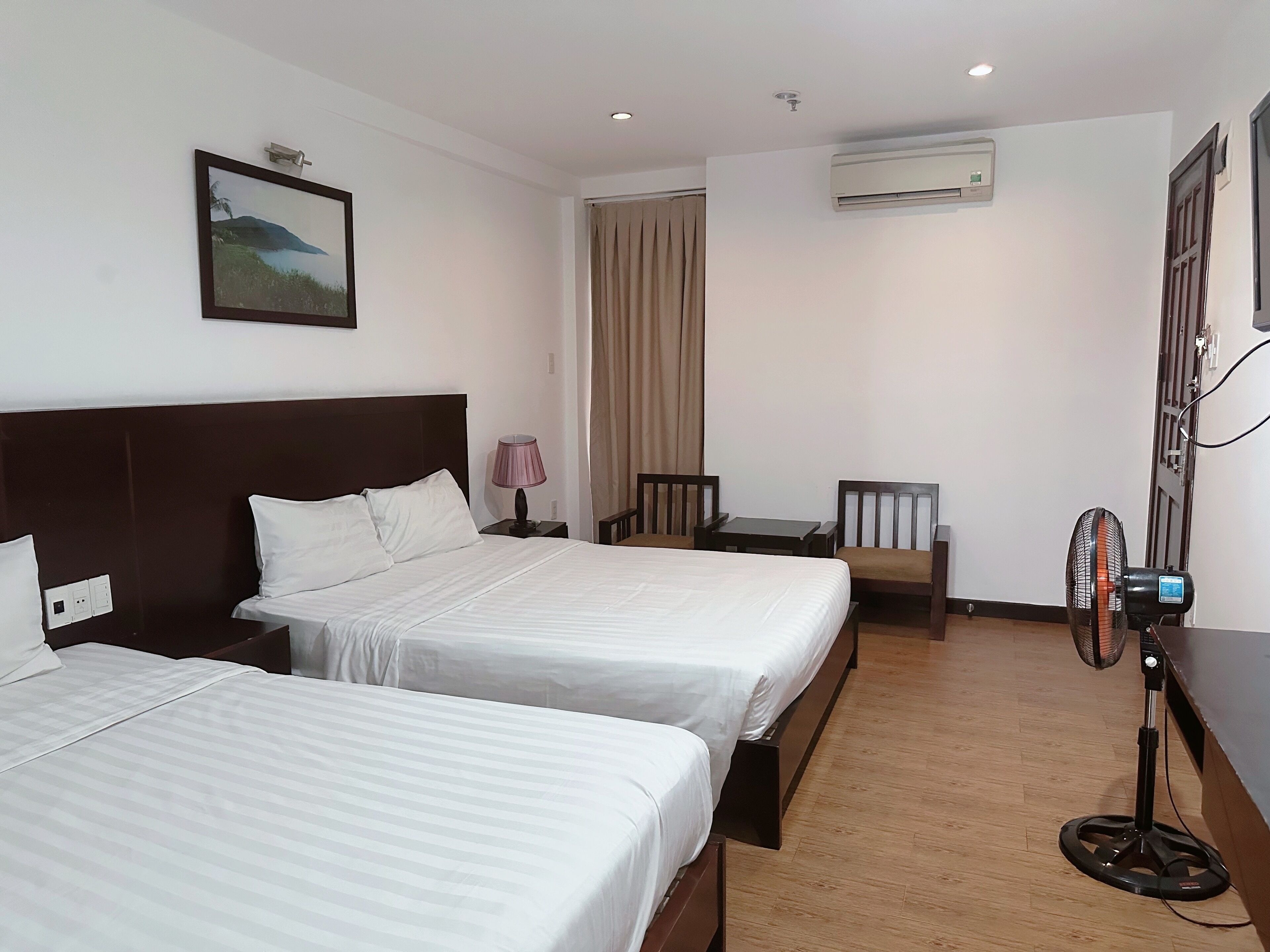A hotel room with two beds, a desk, a chair, an air conditioner, and a fan.