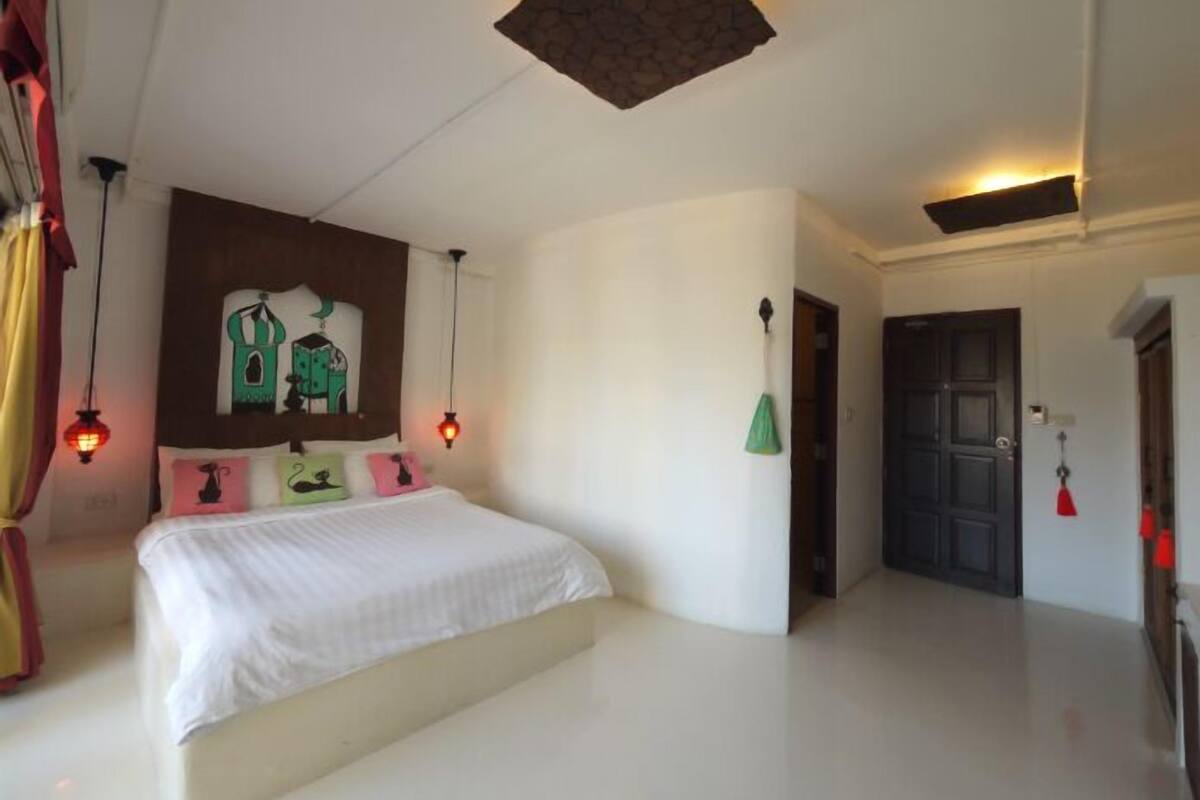 Une chambre à coucher avec un lit, une œuvre d’art accrochée au mur, une porte et un luminaire fixé au plafond.
