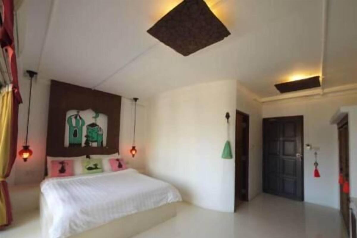 Une chambre à coucher avec un lit, une œuvre d’art accrochée au mur, une porte et un luminaire suspendu.