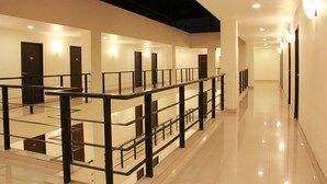 A modern hotel corridor with glass railings, multiple doors, and recessed lighting.