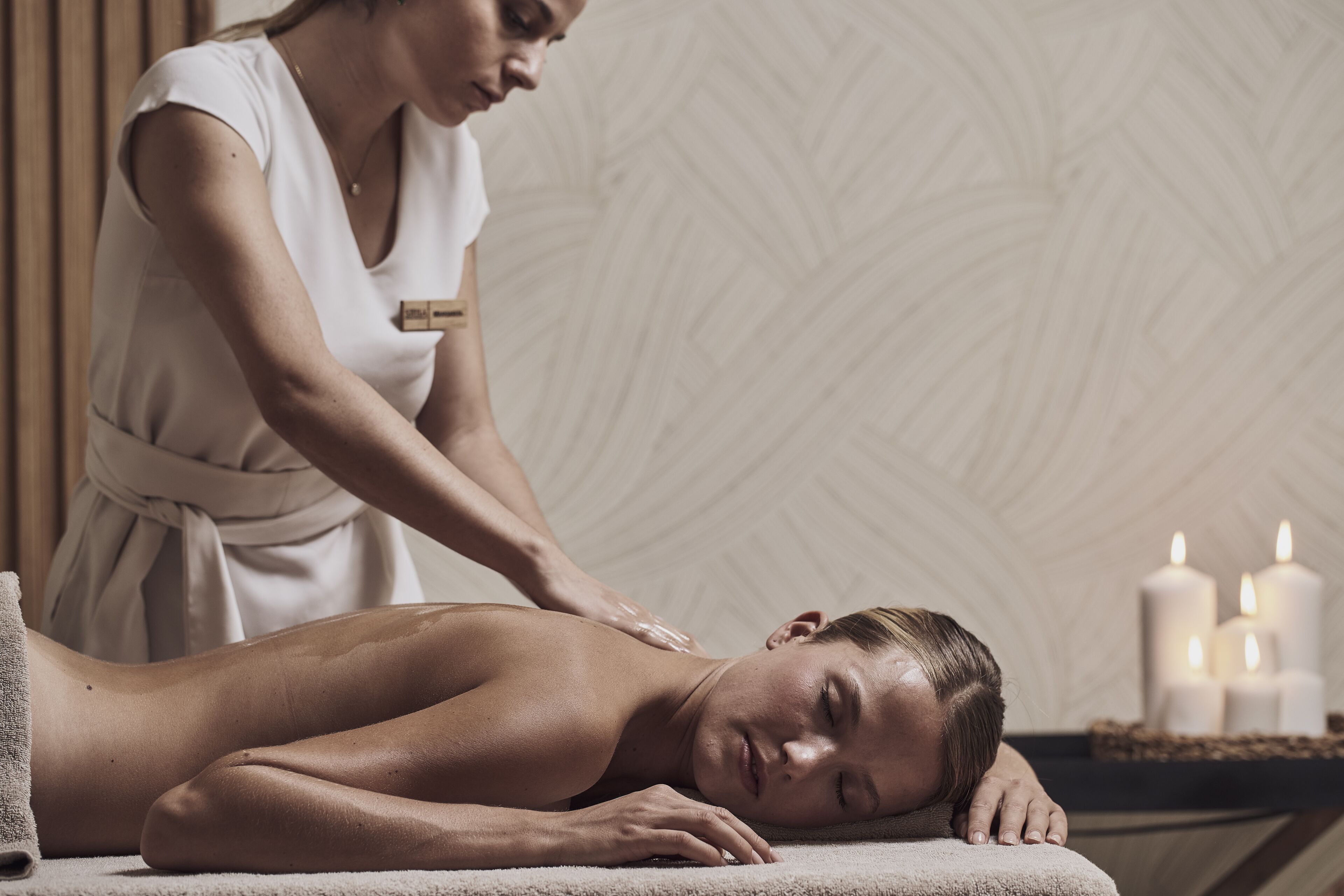 A person receiving a massage in a spa setting with candles and a textured wall in the background.
