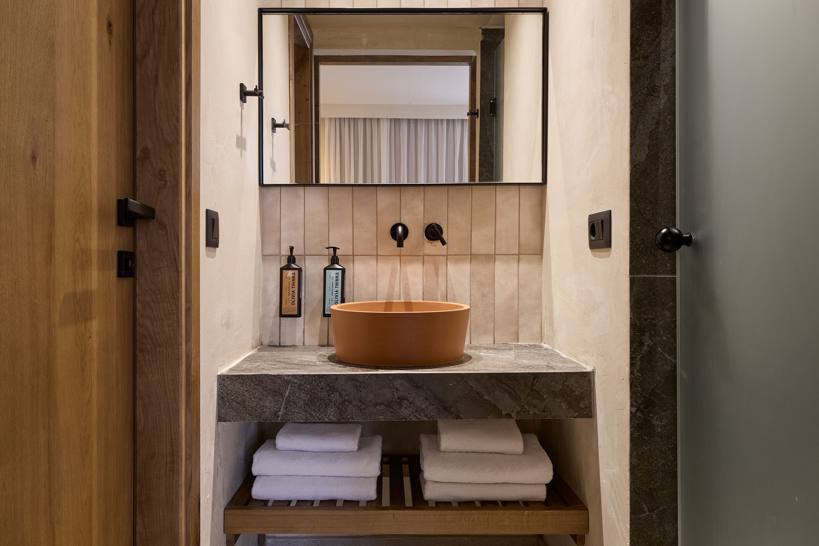 A bathroom with a wooden door, a marble countertop, a large terracotta basin, and a mirror above the sink.