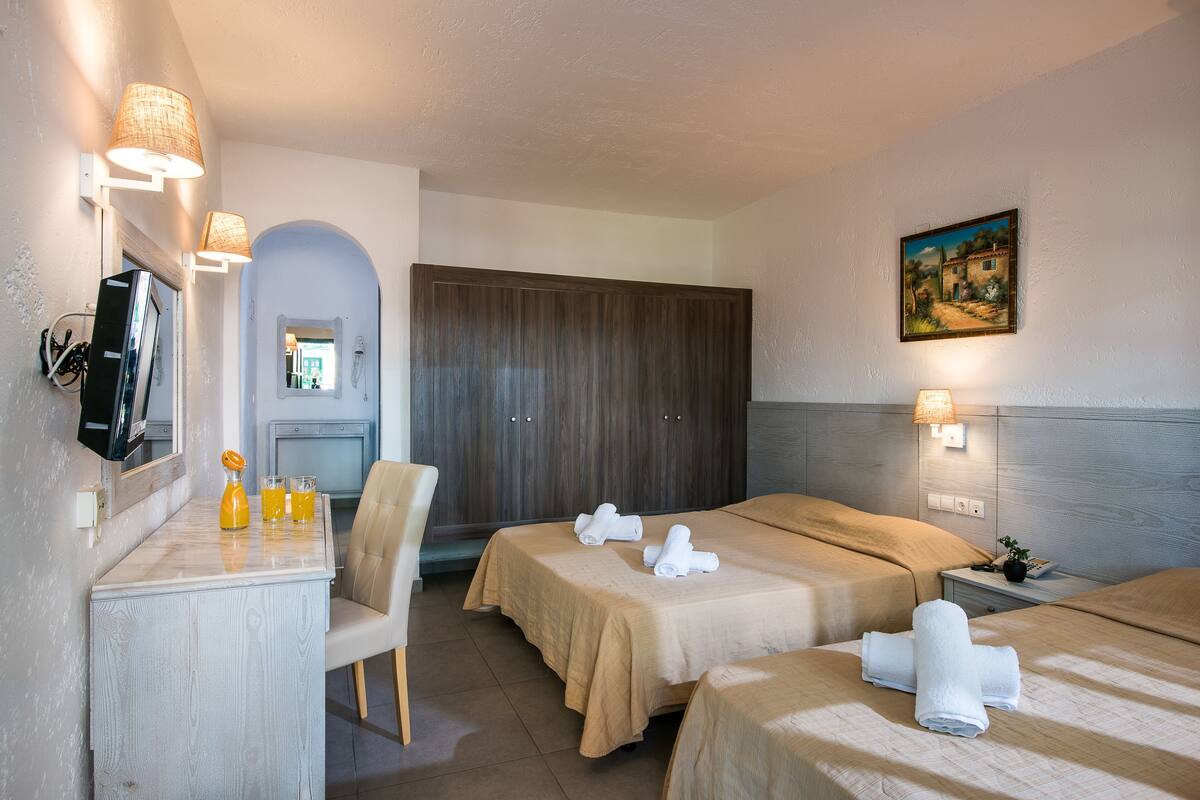 Een hotelkamer met twee bedden, een bureau met stoel, een televisie en een schilderij aan de muur.