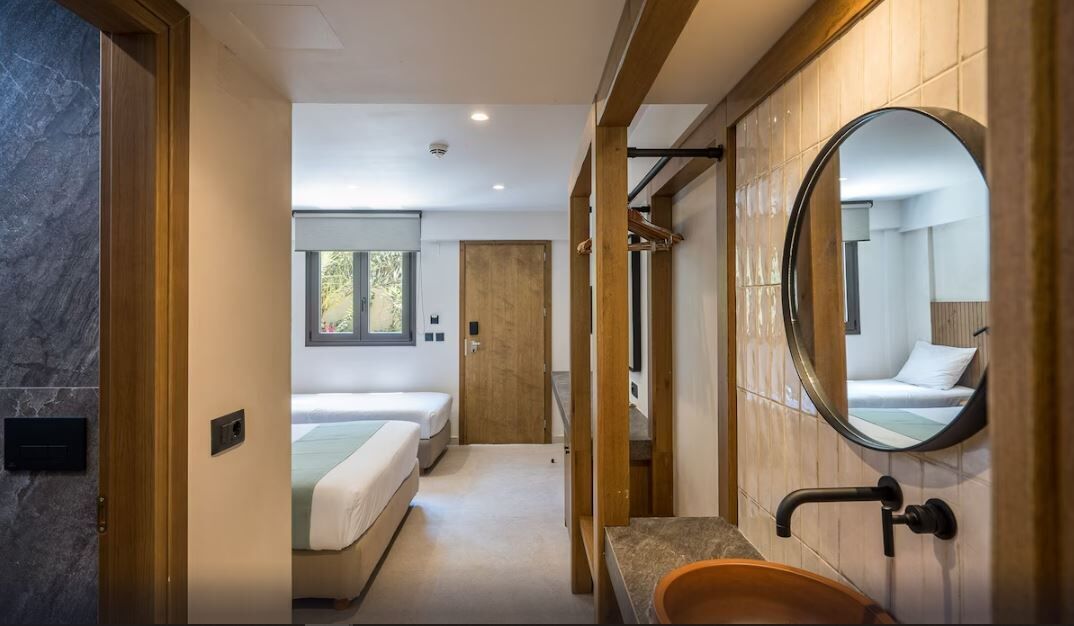 Quarto de hotel moderno com um espelho grande, porta de madeira, cama e banheiro com pia e espelho.