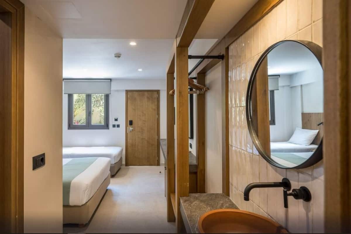 A modern hotel room with a large mirror, a wooden door, a bed, and a bathroom with a sink and mirror.