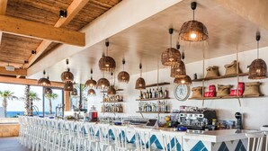 A bar area with white chairs, a counter with various bottles and a clock, and wicker hanging lights. - Stella Village Seaside Hotel - All inclusive (Hersonissos)
