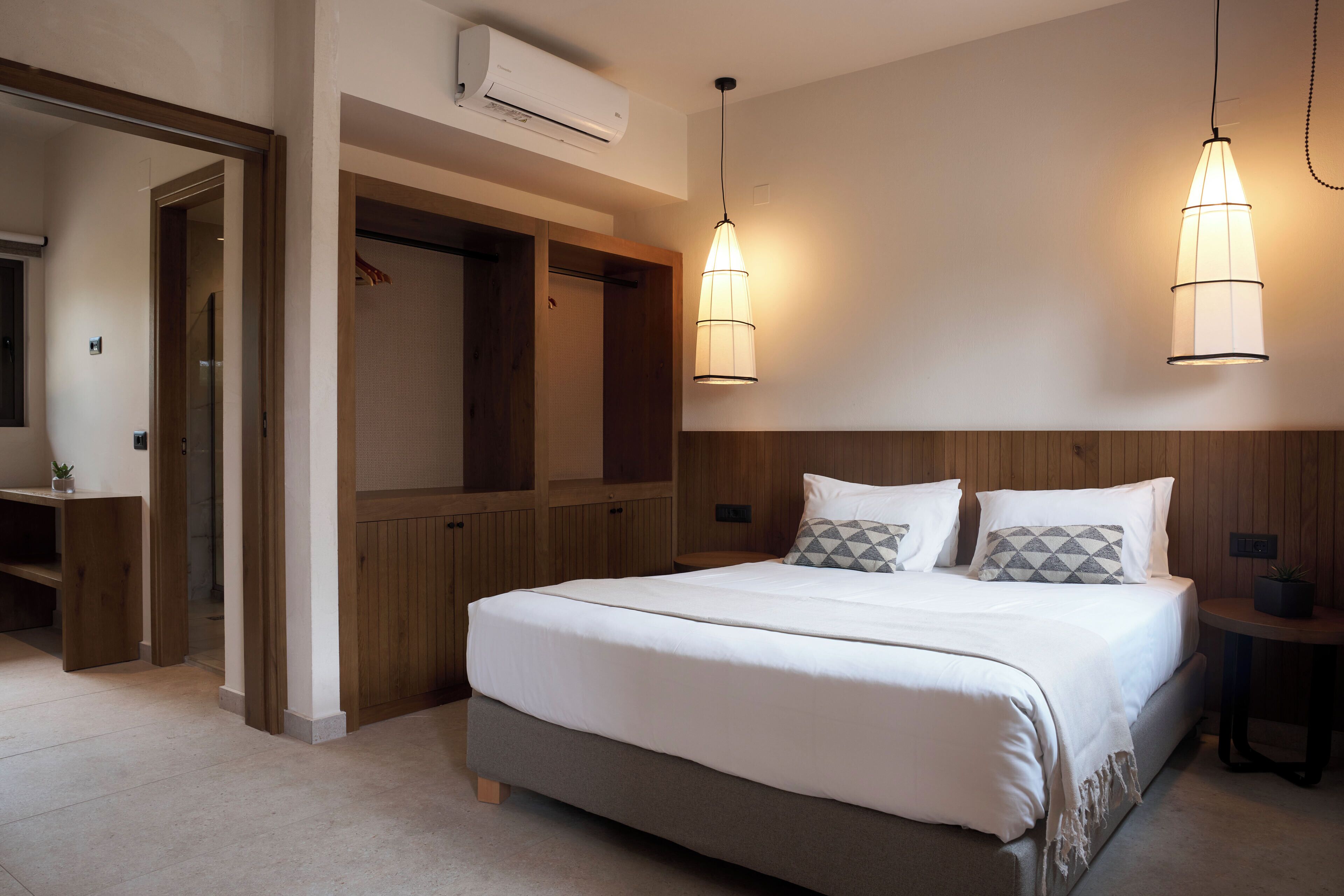 A bedroom with a large bed, wooden headboard, two pendant lights, a bedside table, and a wardrobe.