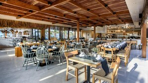 A spacious restaurant with high wooden ceilings and large windows allowing natural light. Tables are set with white tablecloths and centerpieces. - Stella Village Seaside Hotel - All inclusive (Hersonissos)