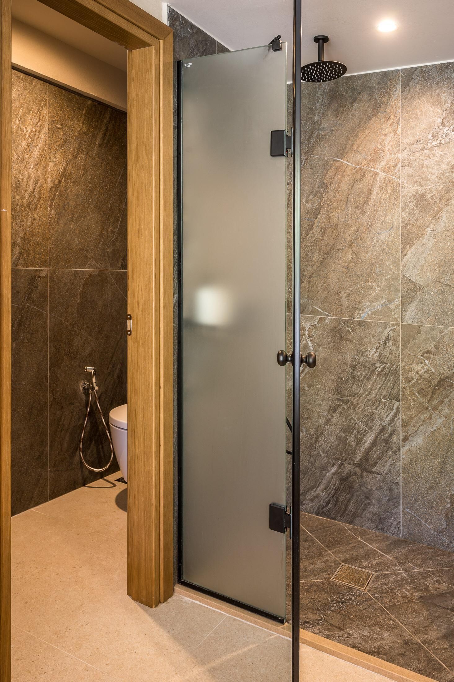 A modern bathroom with a glass shower enclosure, a wooden door, and marble tiles.