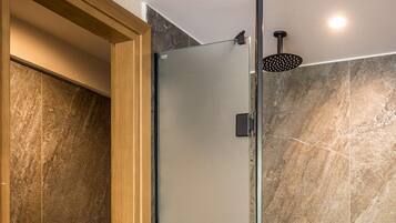 A modern bathroom with a glass shower enclosure, a wooden door, and marble tiles.