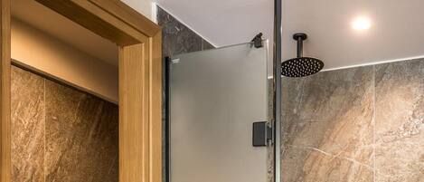Un baño moderno con cabina de ducha de vidrio, puerta de madera y baldosas de mármol.