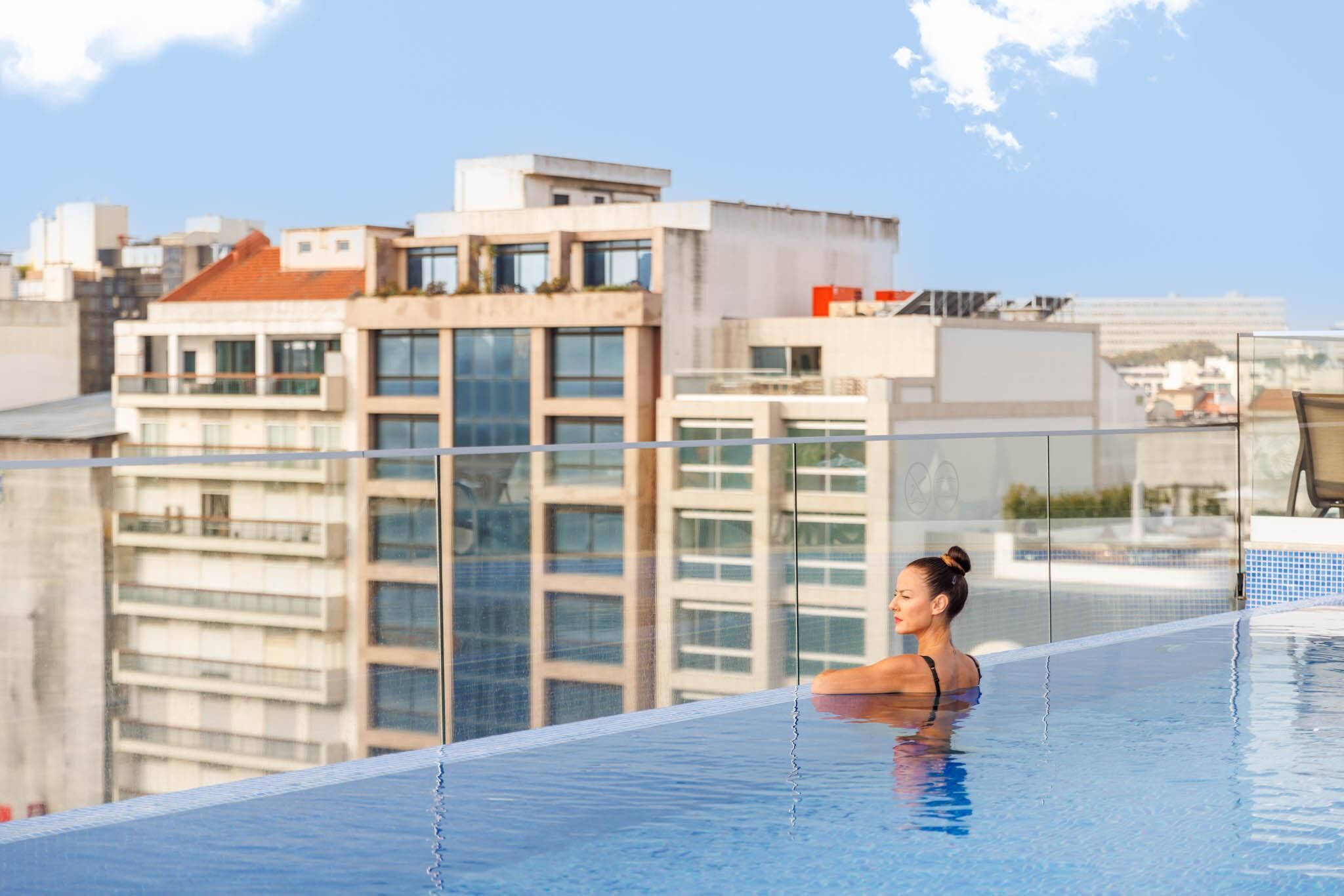 Una persona en una piscina infinita en la azotea, con vista a la ciudad.