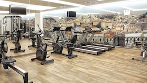 Un gimnasio con diversos equipos de ejercicio y vistas a la ciudad a través de amplias ventanas.