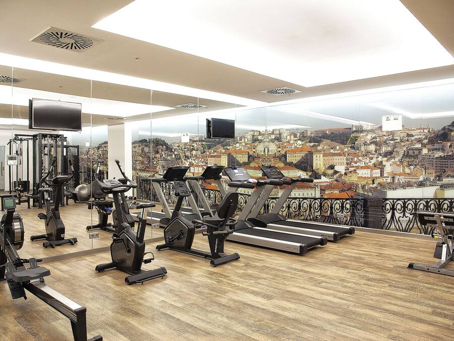 Un gimnasio con diversos equipos de ejercicio y vistas a la ciudad a través de amplias ventanas.