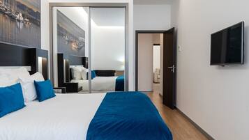 Une chambre d’hôtel dotée d’un grand lit, d’un téléviseur à écran plat, d’une porte coulissante donnant sur une autre pièce et d’une grande fenêtre avec vue sur les bateaux.