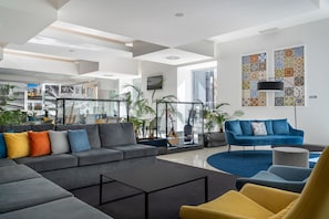 A modern living room with a grey sectional sofa, a yellow armchair, and a blue sofa with a patterned wall behind it.