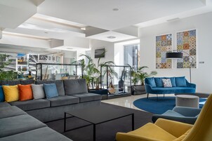 Un salon moderne avec un canapé d’angle gris, un fauteuil jaune et un canapé bleu, le tout devant un mur orné d’un motif.