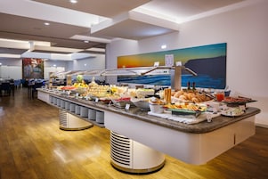 A buffet with various food items and a painting of a sunset over the ocean.