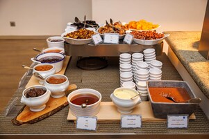 Ein reichhaltiges Buffet mit verschiedenen Speisen und Beilagen, darunter Honig, gezuckerte Milch und Schokoladencreme.