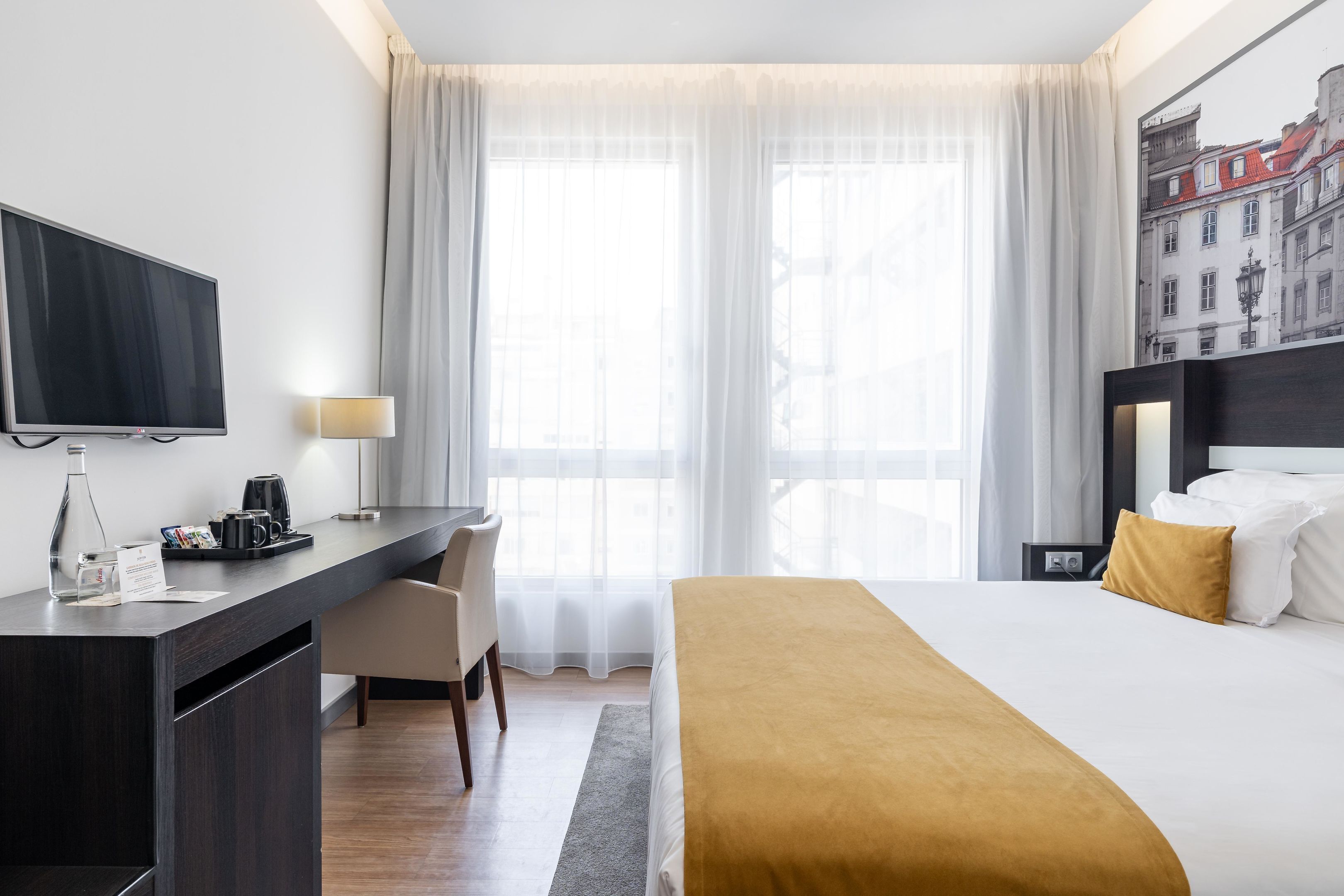 A hotel room with a bed, a desk, a TV, a coffee maker, and a window with curtains.