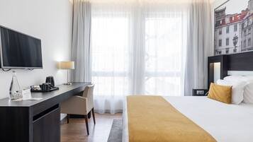 A hotel room with a bed, a desk, a TV, a coffee maker, and a window with curtains.