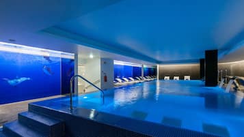 Ein Hallenbad mit klarem, blauem Wasser, Stufen zum Einstieg und Blick auf den Ozean durch die Wände.
