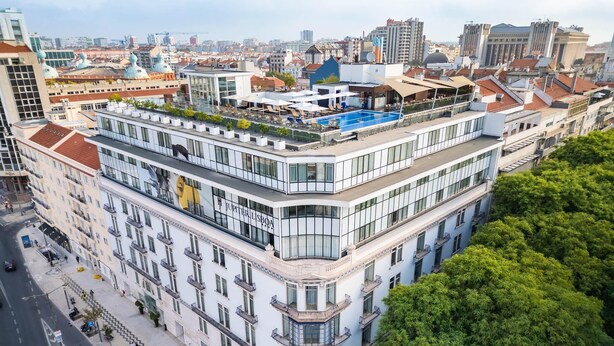 Un hotel de varios pisos con piscina y terraza en la azotea.