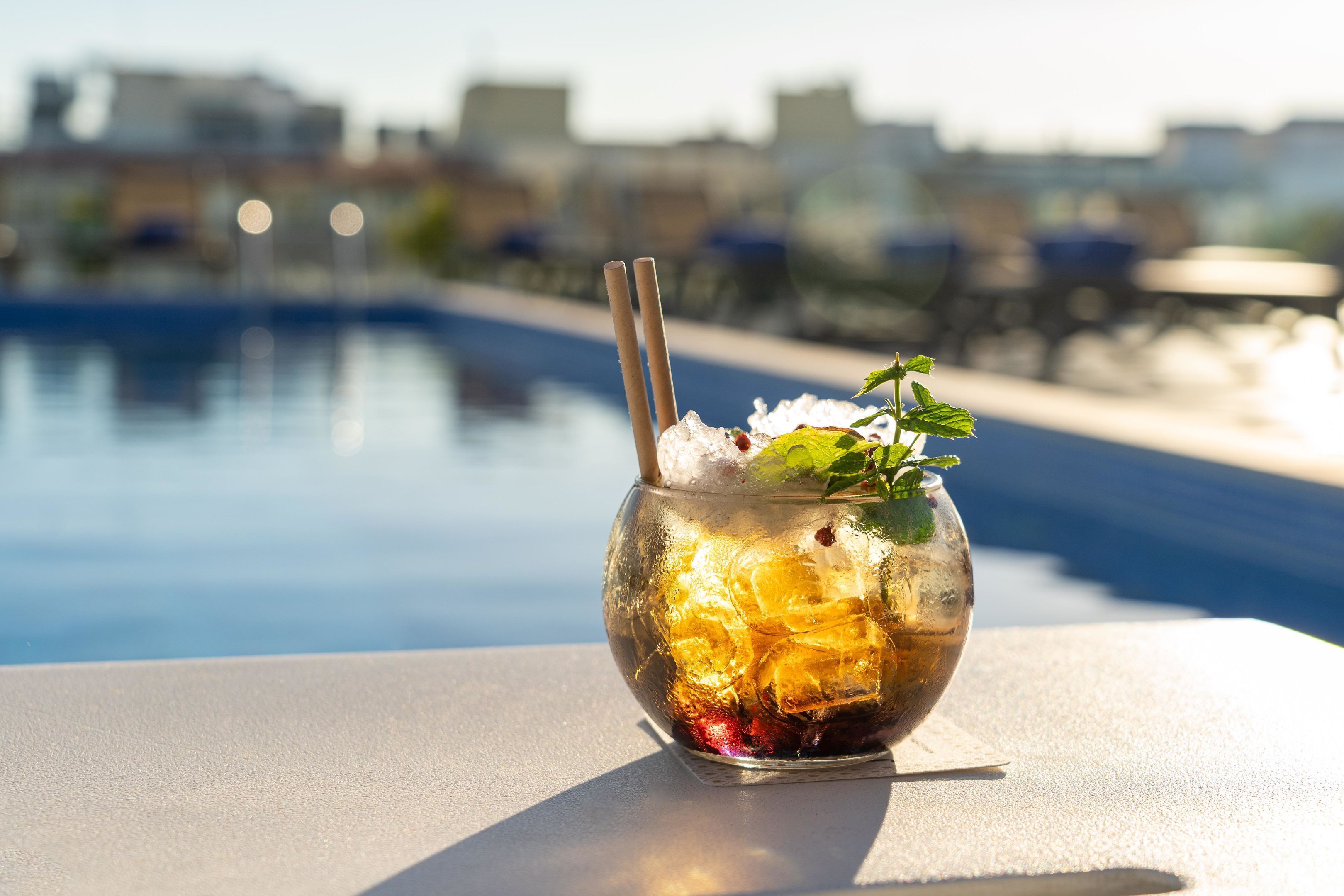 Un vaso con cubitos de hielo y una pajita sobre una mesa junto a la piscina.