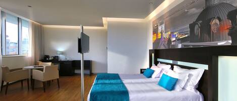A modern hotel room with a large bed, a desk, a chair, and a TV.