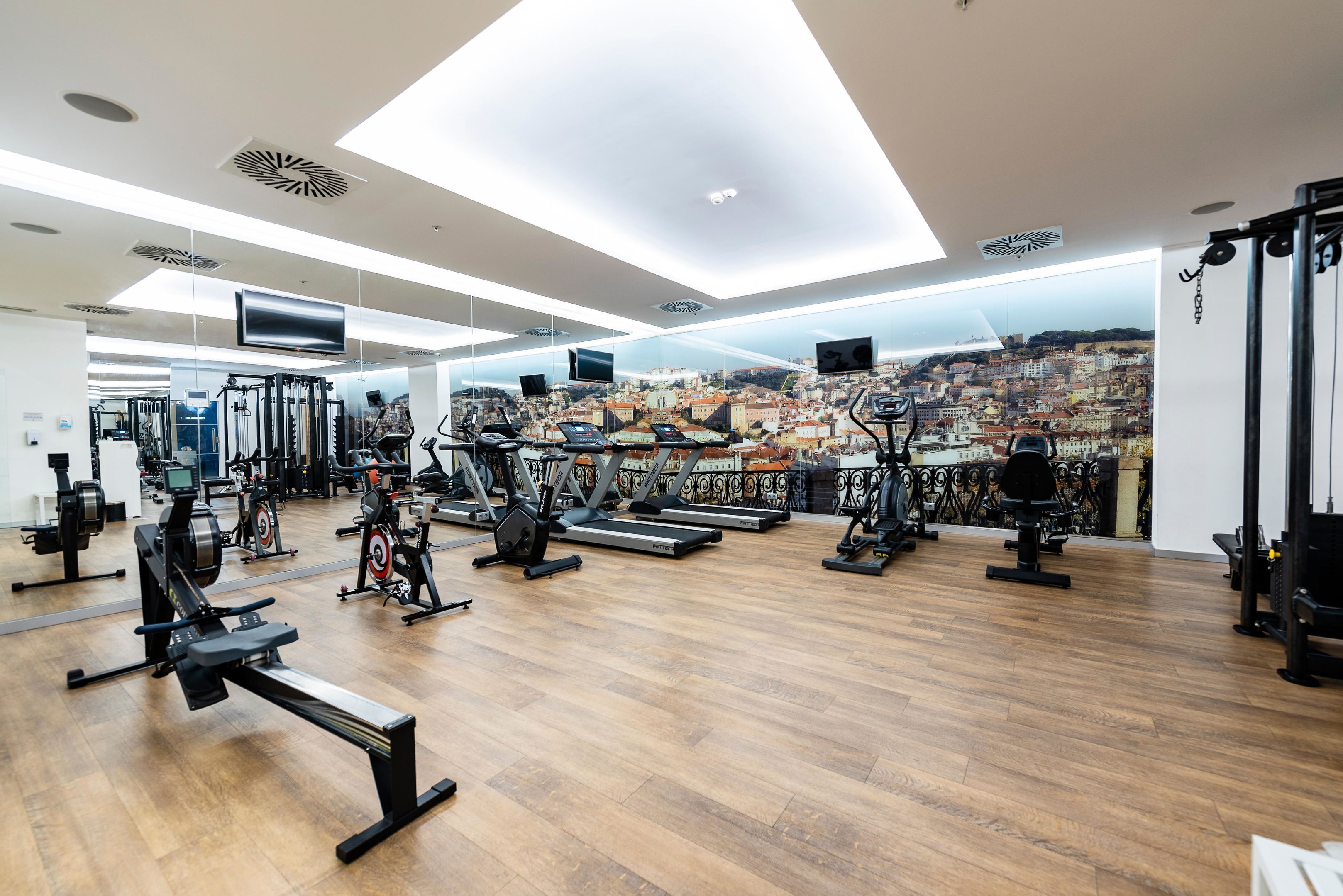 Een fitnessruimte met diverse trainingsapparaten, een stadszicht door grote ramen en een modern plafondontwerp.