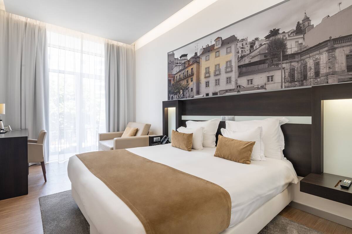 Habitación de hotel con una cama grande, un escritorio, una silla y un cuadro de un paisaje urbano en la pared.
