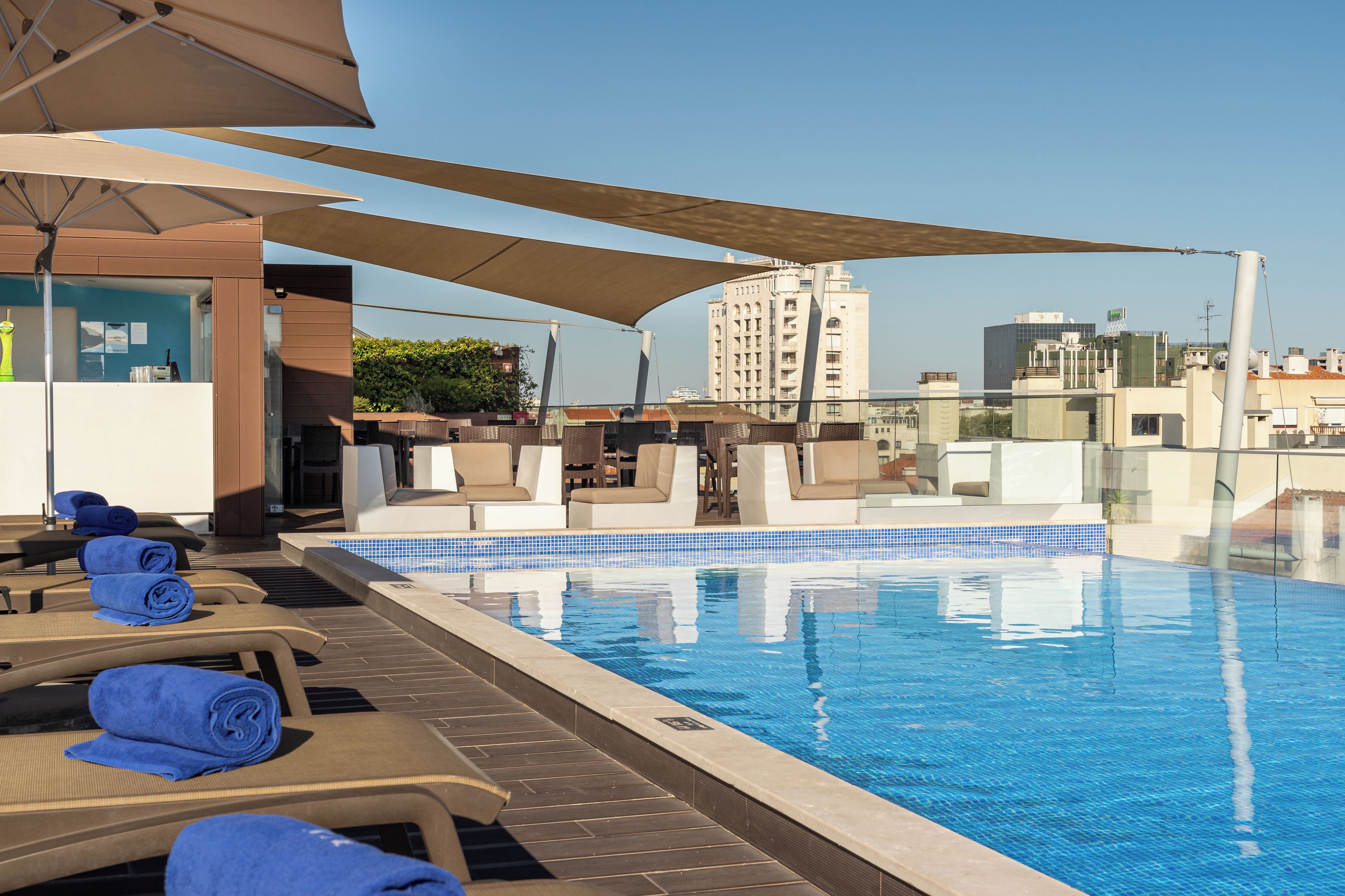Un espace piscine sur le toit, avec des chaises longues et un bar.
