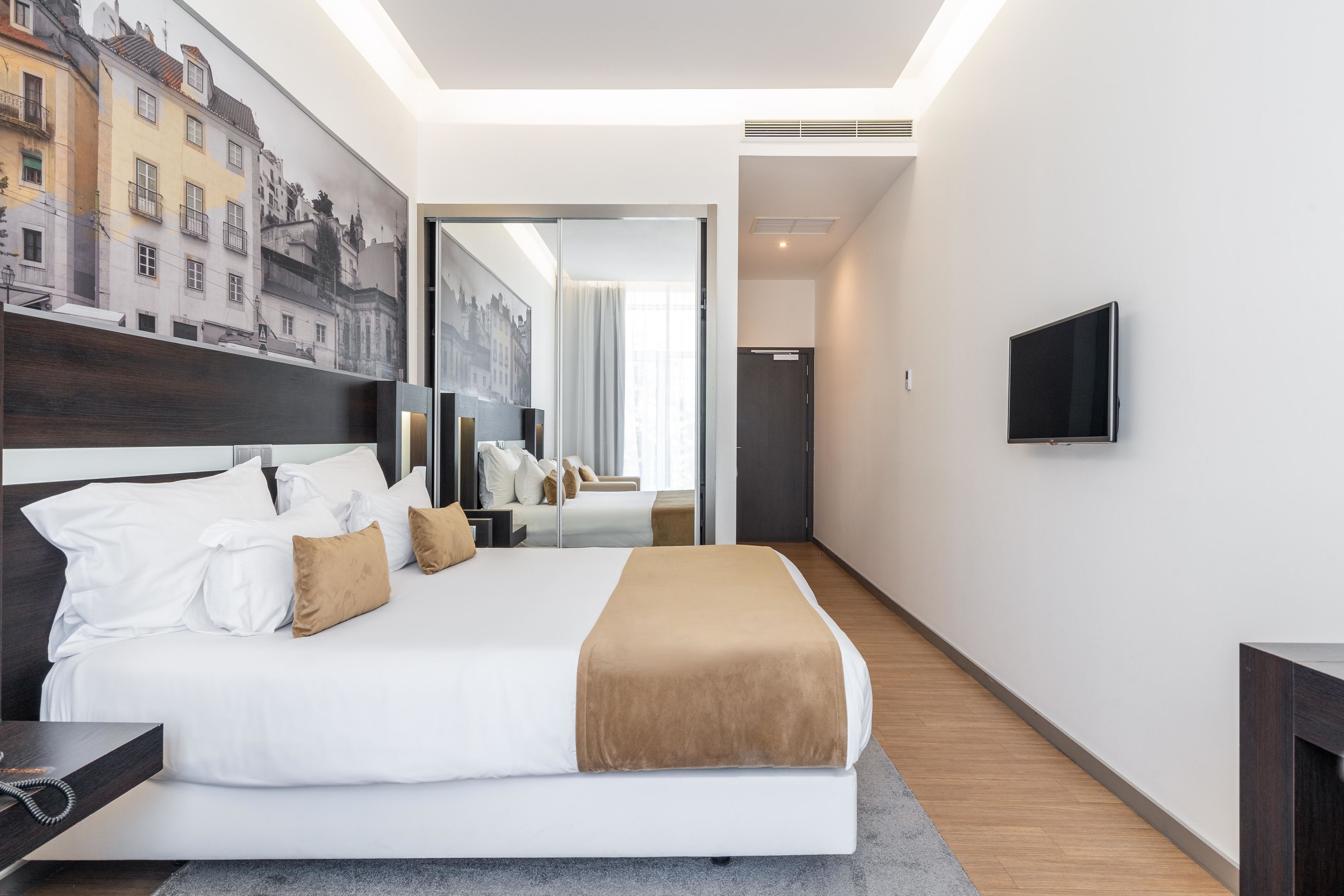 A modern hotel room with a large bed, a flat-screen TV, and a cityscape mural on the wall.