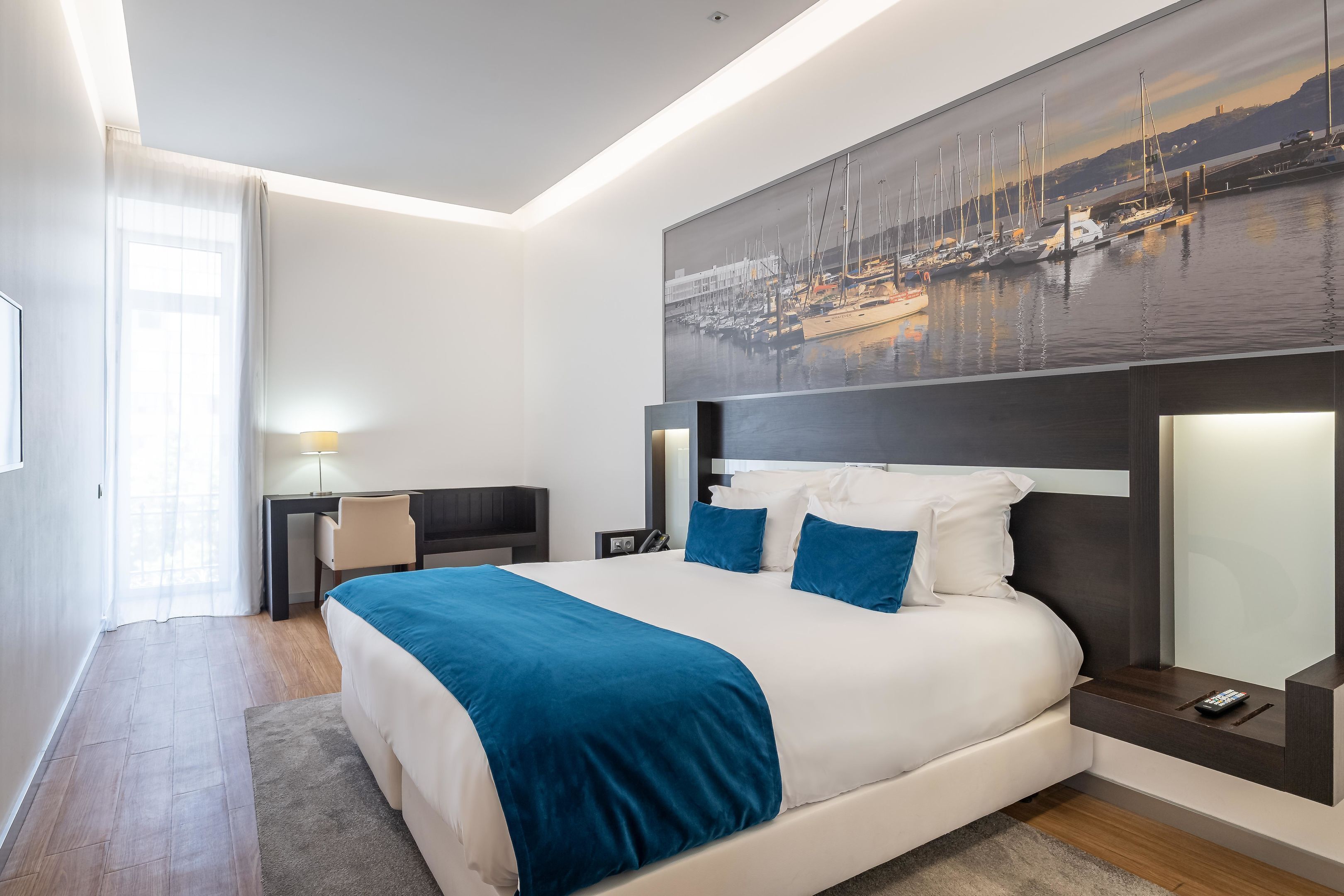 A modern hotel room with a large bed, a desk, and a view of a marina.