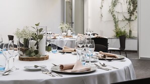 Mesa de comedor dispuesta con mantel blanco, cristalería y un centro de mesa con flores y follaje.