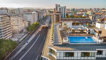A modern building with a rooftop pool, a spacious road, and surrounding urban buildings.