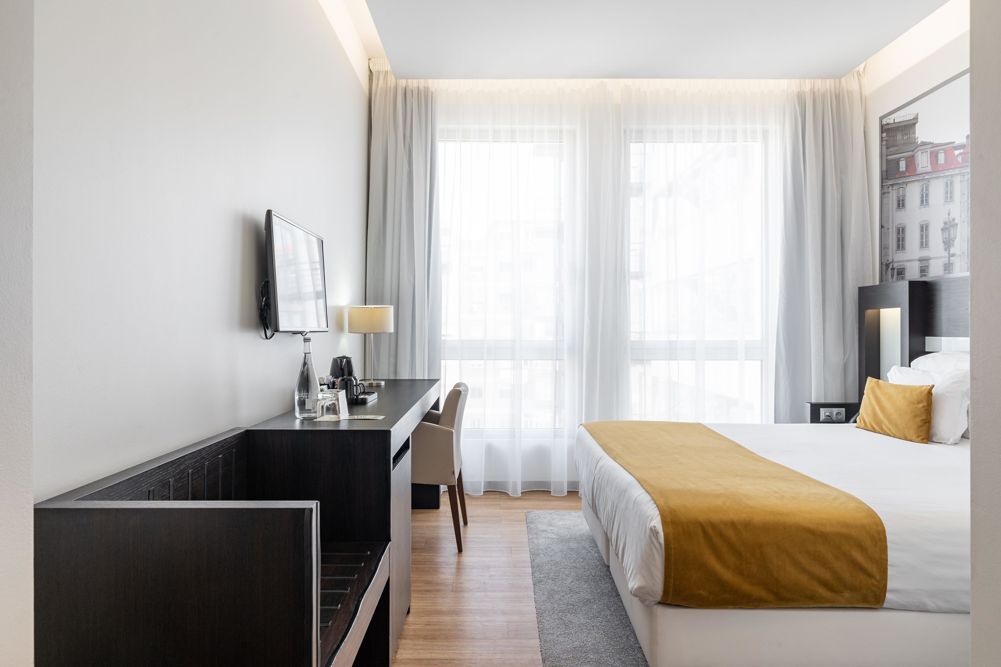 Habitación de hotel con cama, escritorio, silla, televisor y ventana con cortinas.