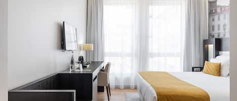 Habitación de hotel con cama, escritorio, silla, televisor y ventana con cortinas.