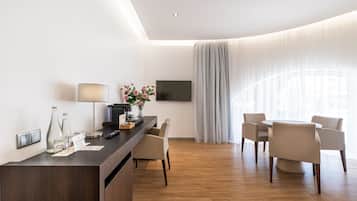 Een moderne hotelkamer met een houten vloer, een ronde eettafel met vier stoelen, een aan de muur bevestigde televisie en een groot raam met dunne gordijnen.