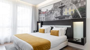 A modern hotel room with a large bed, a nightstand, a mirror, and a wall-mounted artwork of a cityscape.